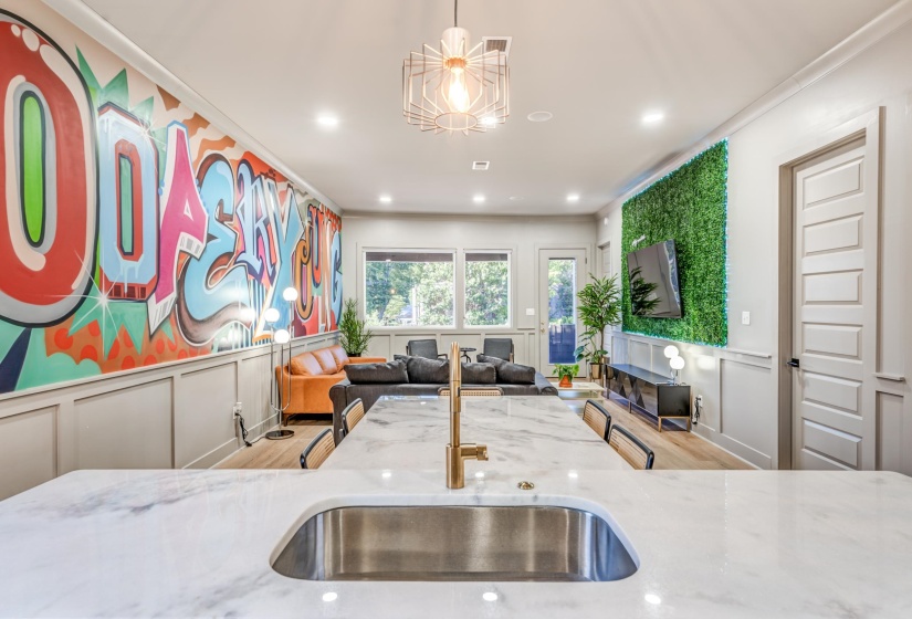 Kitchen featuring light stone counters, wood finished floors, ornamental molding, a decorative wall, and wainscoting