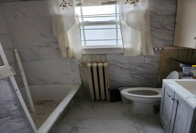 Bathroom with light marble finish floors, vanity, a marble finish shower, radiator heating unit, and tile walls