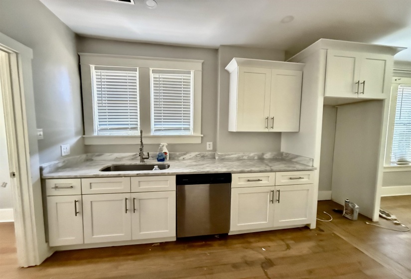 Kitchen with white cabinetry, stainless steel dishwasher, light stone countertops, and dark wood-style floors