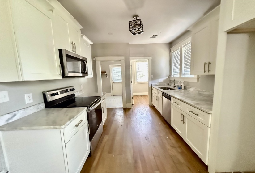 Kitchen with white cabinetry, stainless steel appliances, light countertops, and dark wood-style floors