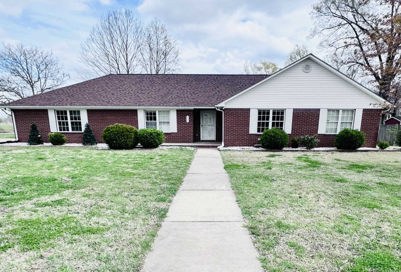 Ranch-style home with roof with shingles, a front yard, and brick siding