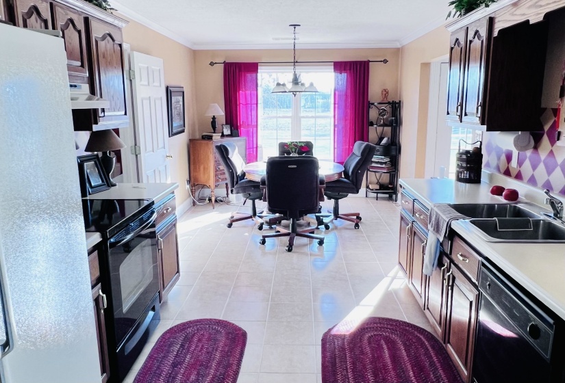 Kitchen featuring black appliances, ornamental molding, light countertops, light tile patterned floors, and range hood