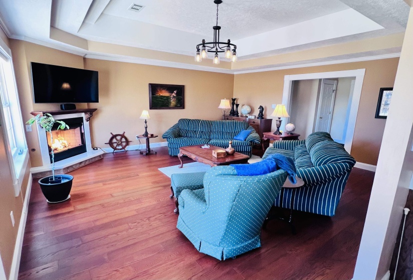 Living room with hardwood / wood-style floors, a tray ceiling, ornamental molding, a warm lit fireplace, and hanging lights