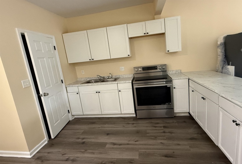 Kitchen with stainless steel electric stove, white cabinetry, light countertops, and dark wood-type flooring