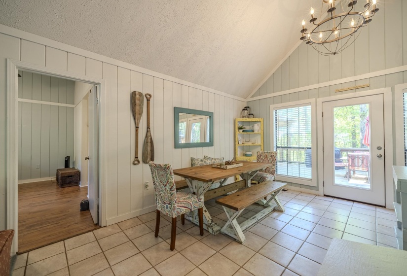 Dining area featuring a vaulted ceiling with a large chandelier, tile flooring, and light-colored vertical wall paneling