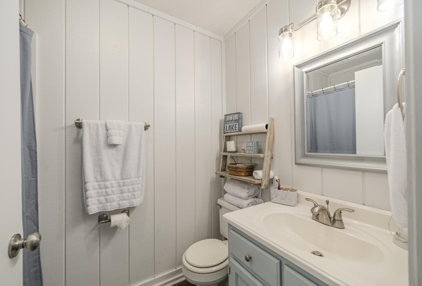 Bathroom featuring vertical paneling, light blue vanity with dual-handle faucet, framed mirror, and brushed nickel light fixture