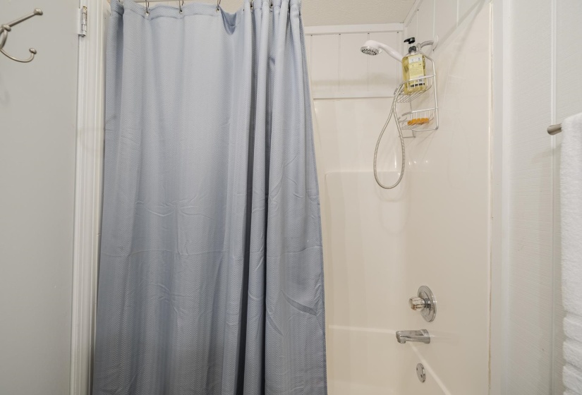 Bathtub and shower combination featuring a flexible shower head, chrome fixtures, and white paneled walls