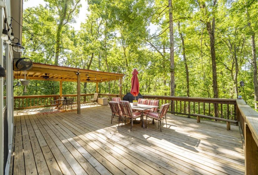 Spacious wood deck featuring a covered pergola, string lighting, and wood railing