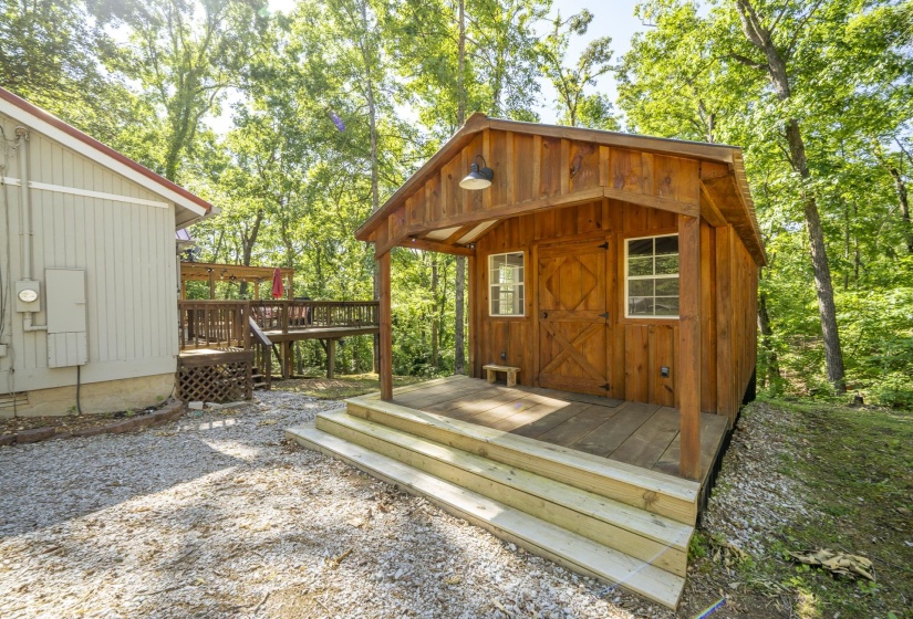 Wood-sided outbuilding featuring a covered porch, two windows, and a barn-style door