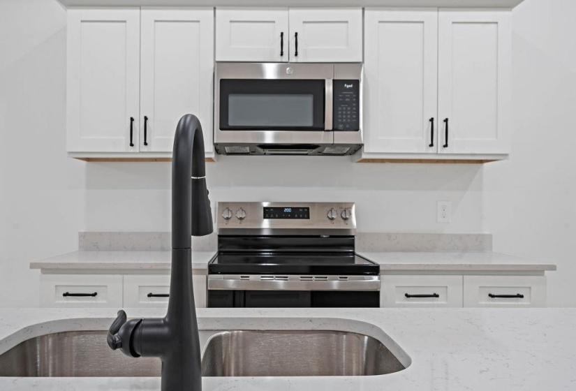 Kitchen with appliances with stainless steel finishes, light stone countertops, and white cabinetry