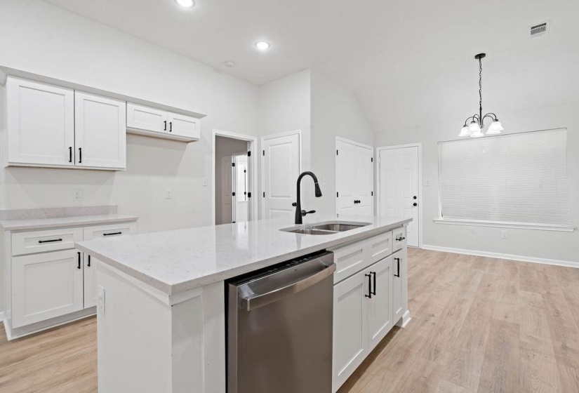 Kitchen featuring light wood finished floors, stainless steel dishwasher, white cabinets, vaulted ceiling, and recessed lighting