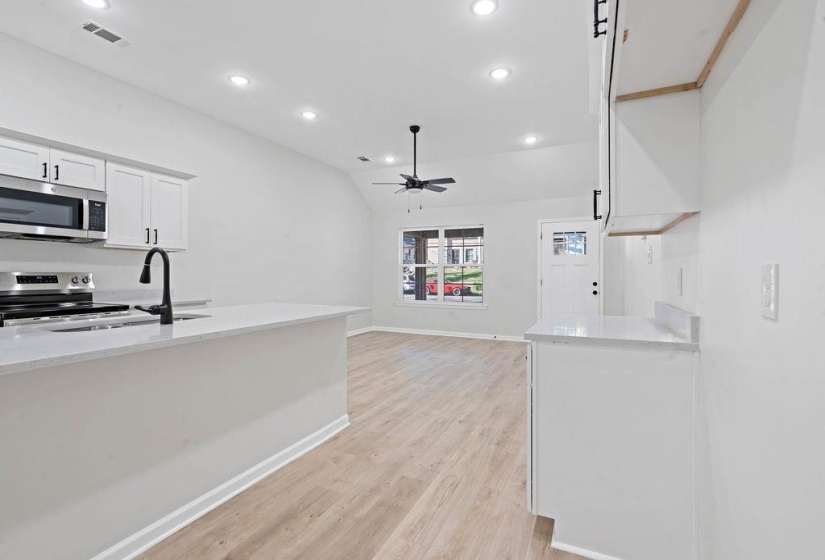 Kitchen with white cabinetry, appliances with stainless steel finishes, vaulted ceiling, recessed lighting, and light stone counters
