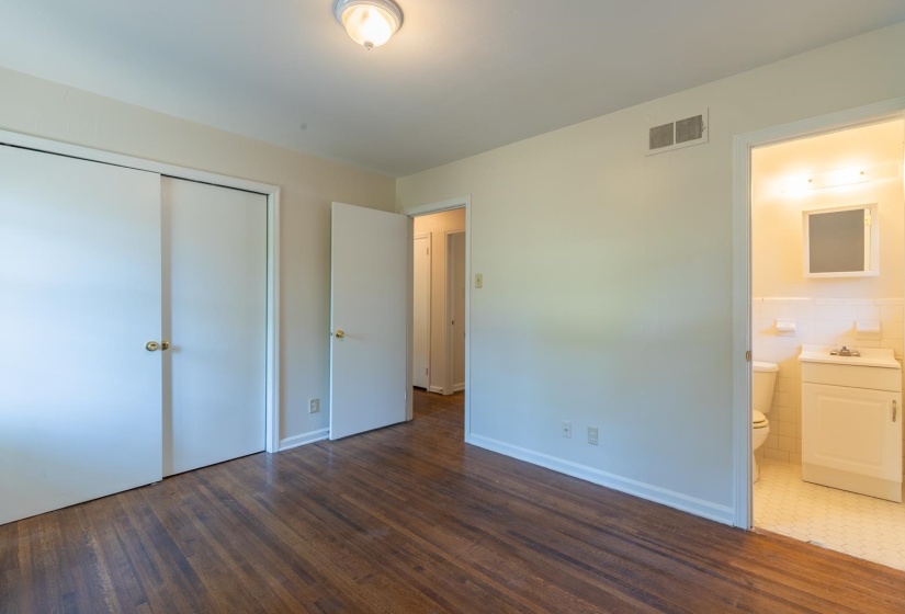 Unfurnished bedroom featuring wood finished floors, a closet, ensuite bath, and baseboards