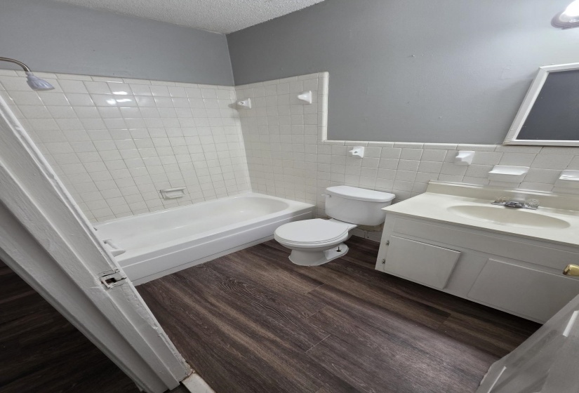 Bathroom featuring vanity, tile walls,  shower combination, dark wood-style flooring, and a textured ceiling