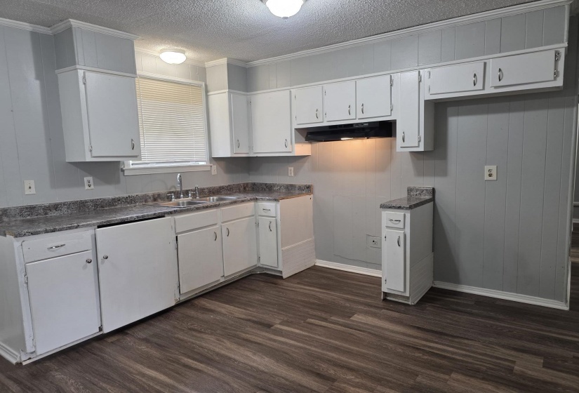 Kitchen featuring a textured ceiling, white cabinetry, dark countertops, dark wood-style floors, and crown molding