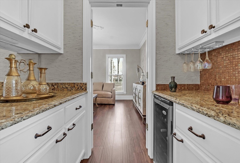 Kitchen featuring white cabinetry, light stone countertops, ornamental molding, beverage cooler, and backsplash