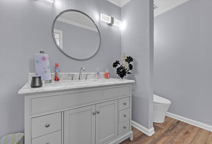 Half bath with vanity, crown molding, and dark wood-style flooring