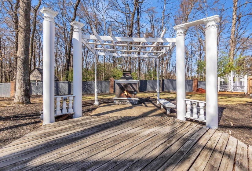 Wooden terrace featuring a fenced backyard, an outdoor stone fireplace, and a pergola