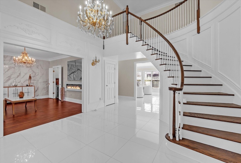 Staircase with suspended lighting, ornamental molding, a high ceiling, a glass covered fireplace, and tile patterned floors