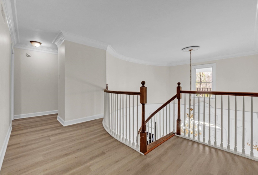 Hall with light wood finished floors, crown molding, and an upstairs landing