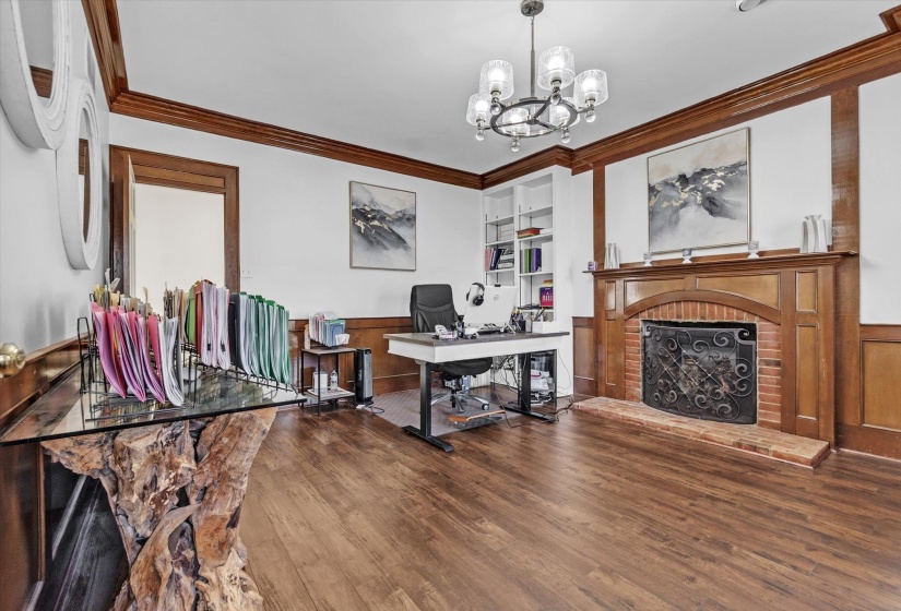 Office area featuring a fireplace, dark wood-style floors, wainscoting, crown molding, and a chandelier
