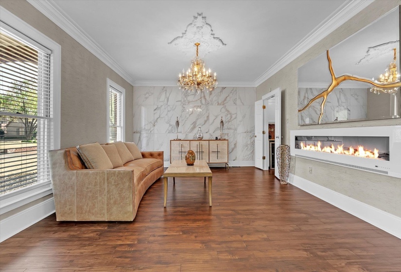 Living area with a chandelier, a glass covered fireplace, ornamental molding, dark wood-style floors, and a textured wall