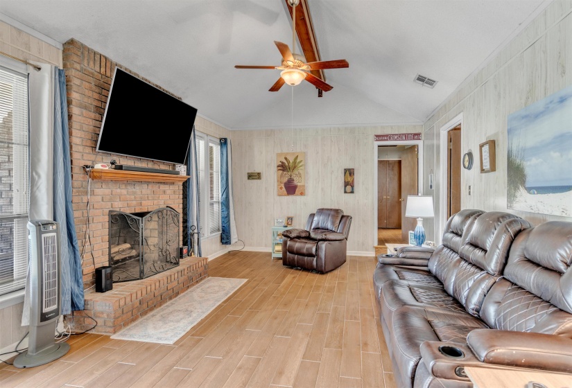 Living room with wood finish floors, a fireplace, beamed ceiling, ceiling fan, and wooden walls