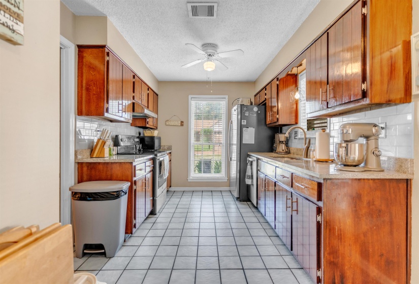 Kitchen with stainless steel appliances, a ceiling fan, light tile patterned flooring, wood finish cabinets, and a textured ceiling