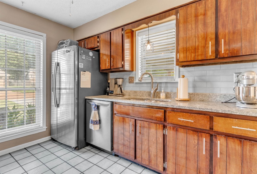 Kitchen with wood finish cabinets, dishwasher, light tile patterned floors, light granite countertops, and decorative backsplash