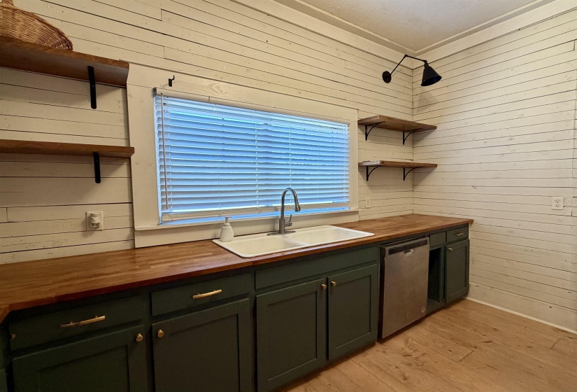 Kitchen featuring wooden counters, open shelves, wood walls, stainless steel dishwasher, and green cabinetry