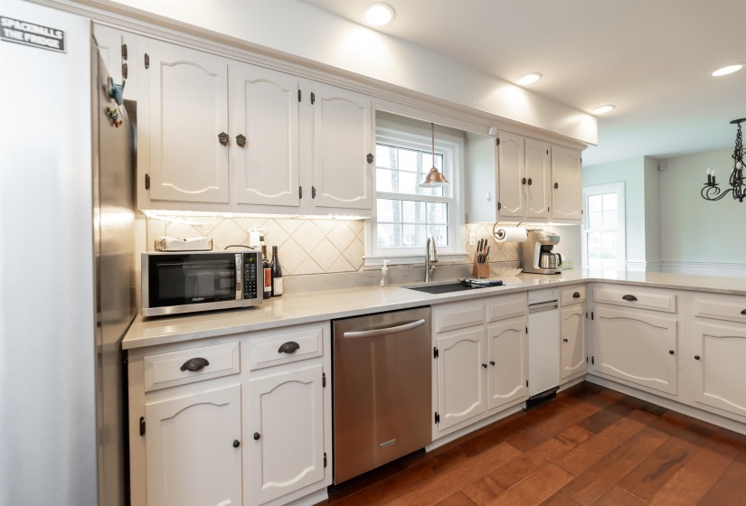 Kitchen with stainless steel appliances, white cabinets, dark wood-style floors, and light stone counters