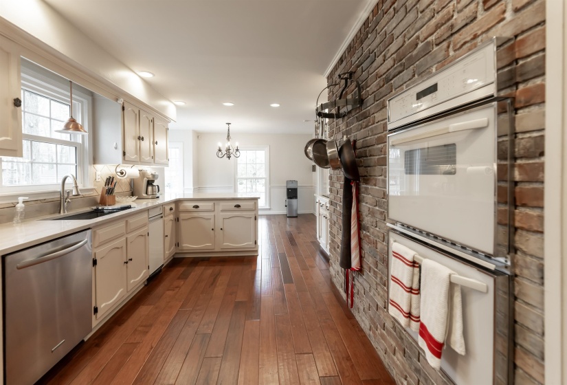 Kitchen with double oven, a peninsula, stainless steel dishwasher, dark wood-style flooring, and a chandelier