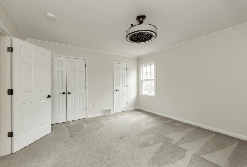 Unfurnished bedroom featuring light carpet, crown molding, and two closets