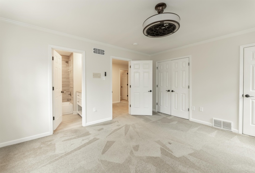 Unfurnished bedroom with light carpet, ornamental molding, ensuite bath, and a ceiling fan
