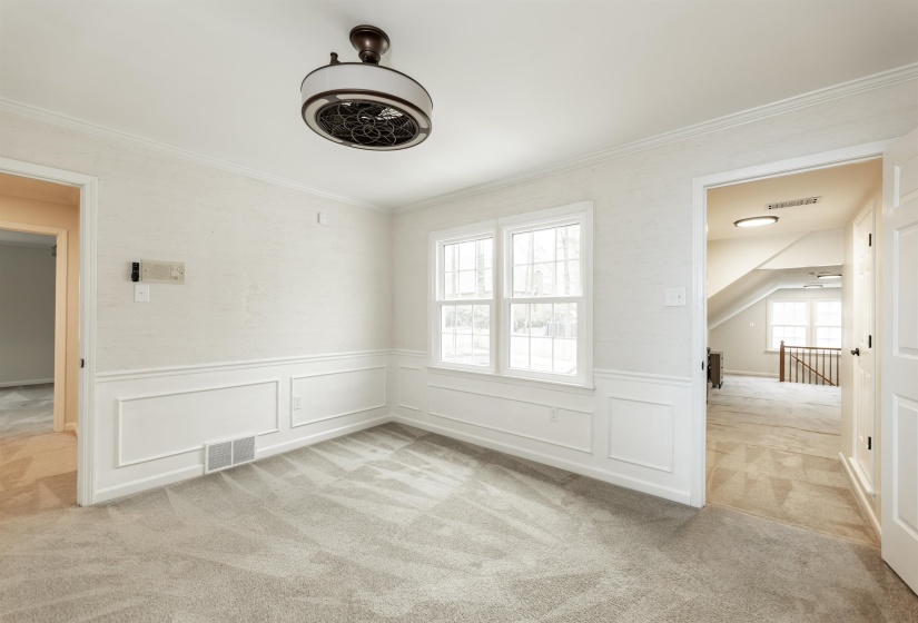 Empty room featuring light colored carpet, a decorative wall, wainscoting, and crown molding