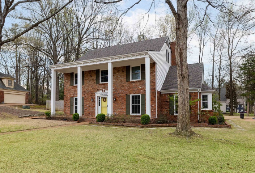 Greek revival house featuring a porch, roof with shingles, brick siding, and a front yard