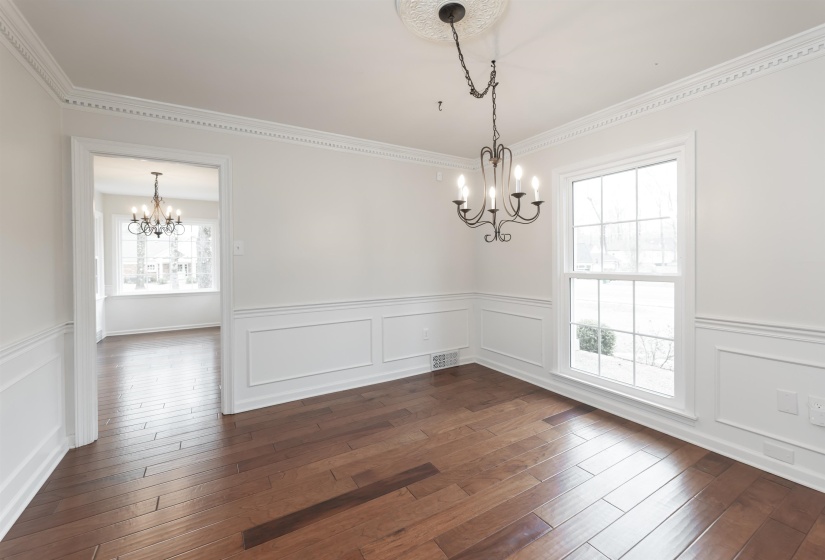 Unfurnished dining area with hanging lights, wainscoting, dark wood-style flooring, a decorative wall, and ornamental molding