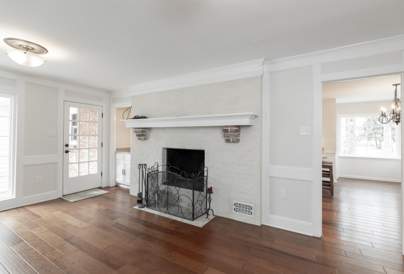 Unfurnished living room with dark wood-style flooring, a decorative wall, a fireplace with flush hearth, crown molding, and suspended lighting
