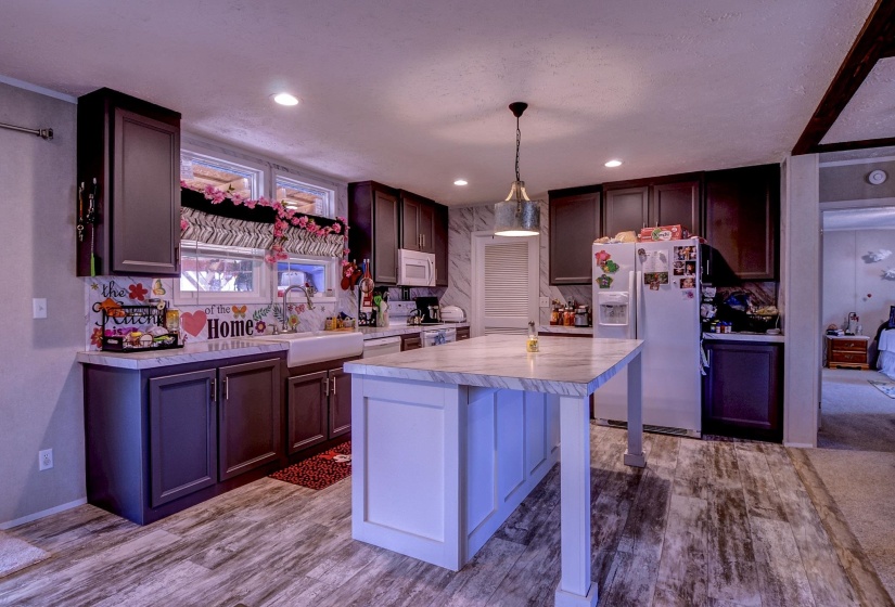 Two tone kitchen featuring light countertops, a breakfast bar area, white appliances, pendant lighting, and a kitchen island