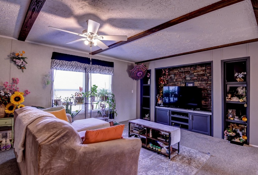Living room featuring a ceiling fan, a textured ceiling, built in shelves, carpet, and crown molding