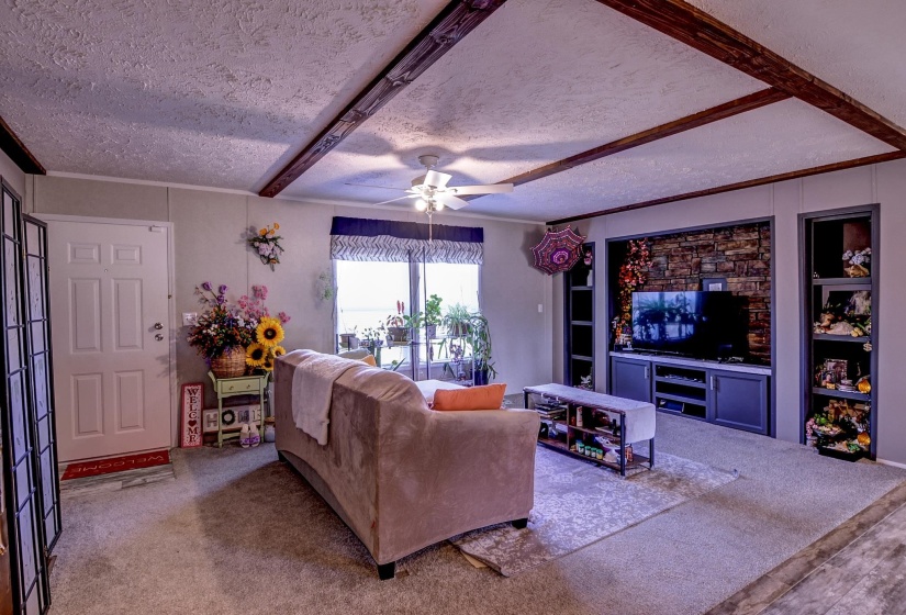 Carpeted living room featuring a textured ceiling, ceiling fan, built in shelves, and beam ceiling