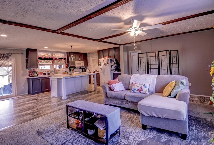 Living room featuring a textured ceiling, wood finished floors, a ceiling fan, and beamed ceiling