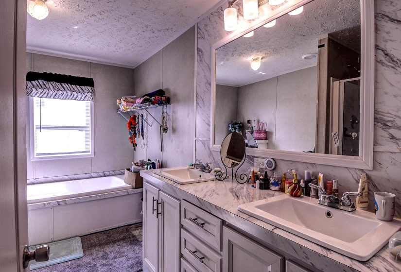 Full bathroom featuring a textured ceiling, double vanity, a shower stall, and a garden tub