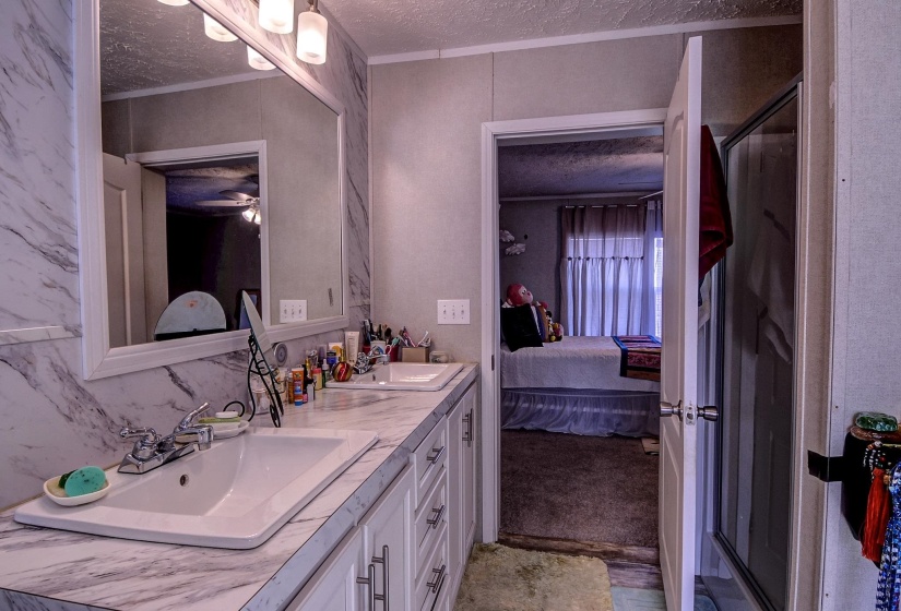 Ensuite bathroom with a textured ceiling, double vanity, and a stall shower