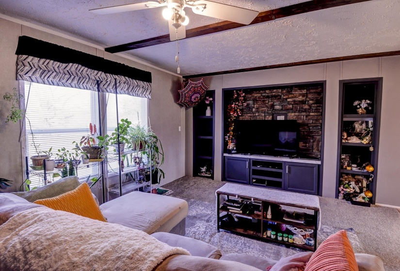 Living area with ceiling fan, carpet, a textured ceiling, crown molding, and built in features