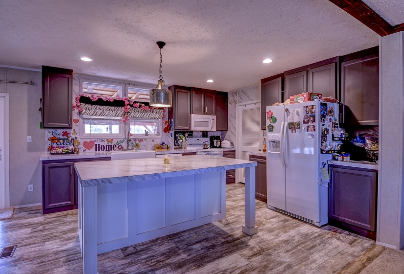 Kitchen with white appliances, pendant lighting, light wood-style floors, a center island, and a textured ceiling