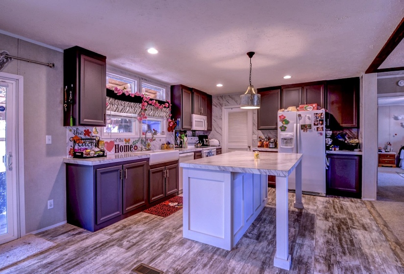 Dual tone kitchen with light countertops, white appliances, a breakfast bar, dark wood-type flooring, and hanging light fixtures