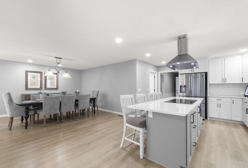 Dual tone kitchen featuring a kitchen island, island exhaust hood, backsplash, a breakfast bar, and light wood-style flooring