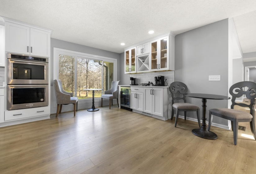 Coffee bar featuring white cabinets, glass fronted cabinets, stainless steel double oven, recessed lighting, and beverage cooler
