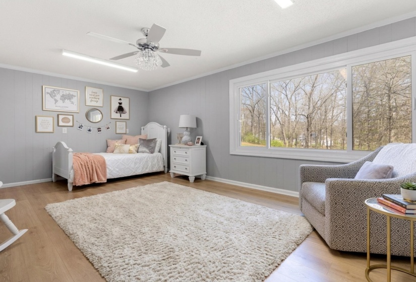 Bedroom featuring light wood-style floors, a ceiling fan, wooden walls, and crown molding